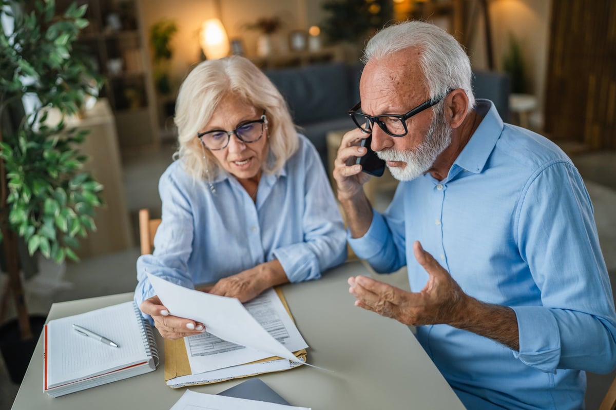 Senior couple looking at documents and making a stressful phone call, managing bills and expenses together while dealing with frustrating administrative tasks